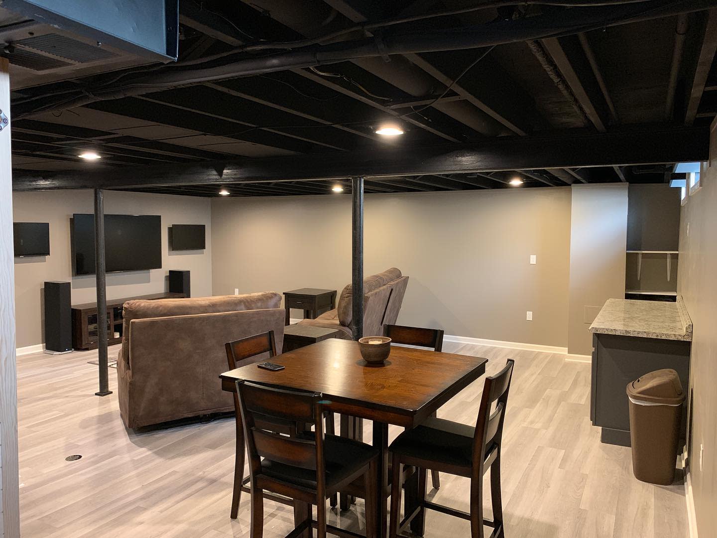 Simple basement living space with entertainment setup, brown seating, and dining table.